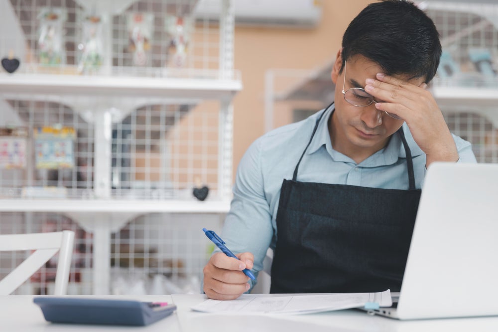 Male Store Owner/Clerk Rubbing Forehead in Distress