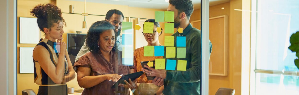 A group of colleagues are standing in an office and posting sticky notes on the wall to make a critical business decision.