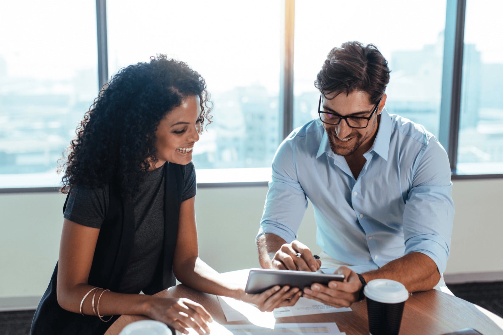 two coworkers look at tablet at small office table